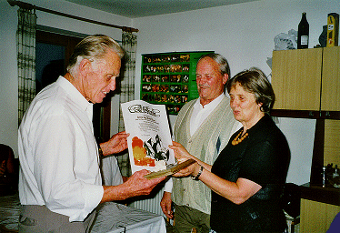 Marianne und Toni übergeben an Rudi die Jubiläumsurkunde und die Holztafel mit Bergkristall.