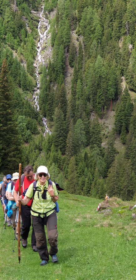 Wandern über eine Wiese, im Hintergrund ein Wasserfall